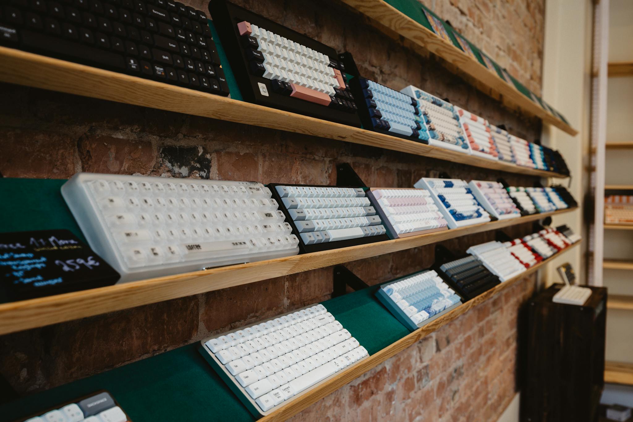 About A variety of mechanical keyboards neatly displayed on a shelf in a brick-walled store interior.